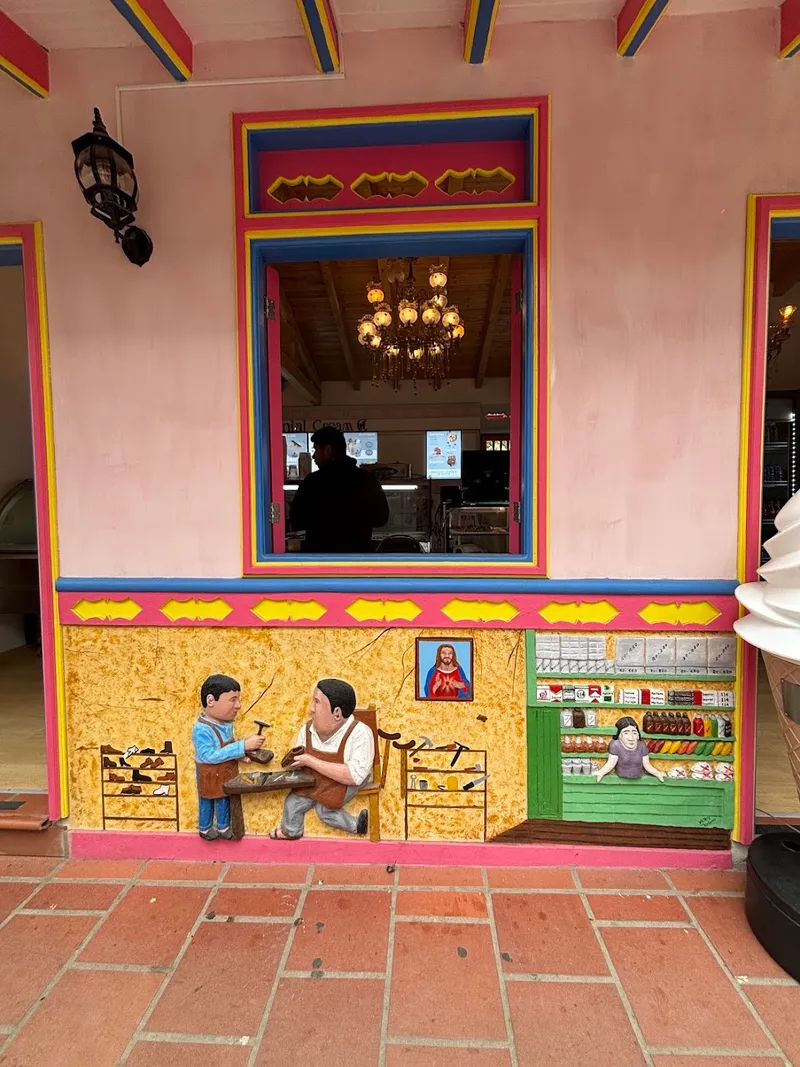A colorful carved mural of a shoemaker and a corner shop on a pink wall in Colombia